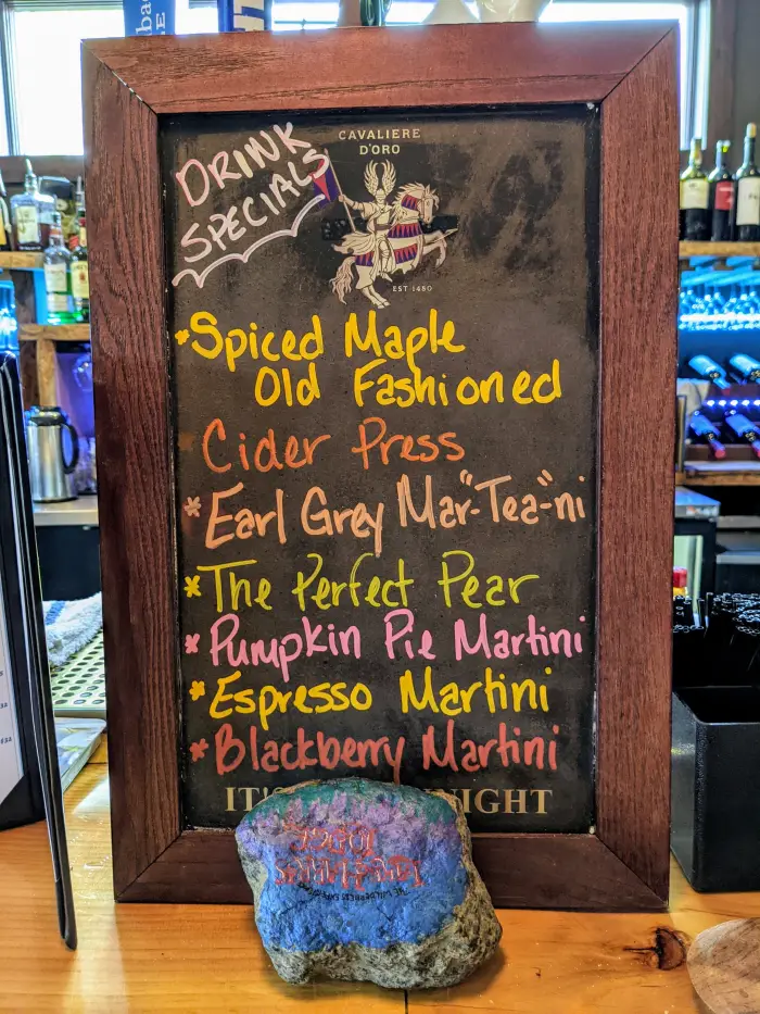 A list of cocktails is written on a chalkboard and displayed on a bar