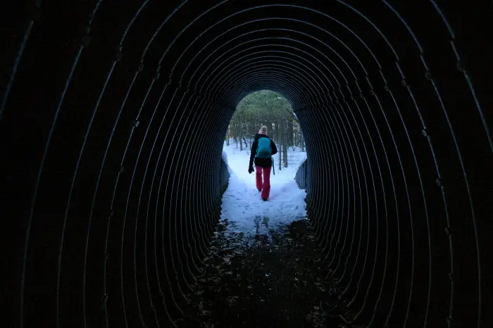 A hiker exits a large metal tunnel that runs under the Northway and provides access to the wilderness.