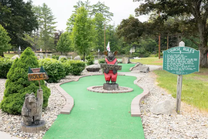 The start of an Adirondack mini golf course&#44; surrounded by pine trees and featuring a carved bear.