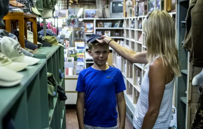 A mom puts a hat on her son in a store.