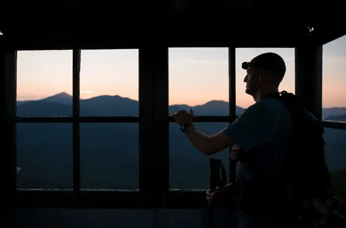 A man looks out of the Goodnow fire tower window in Newcomb at sunrise