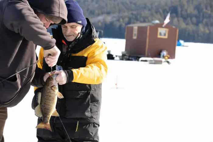 Two guys taking the hook out of a fish on the ice