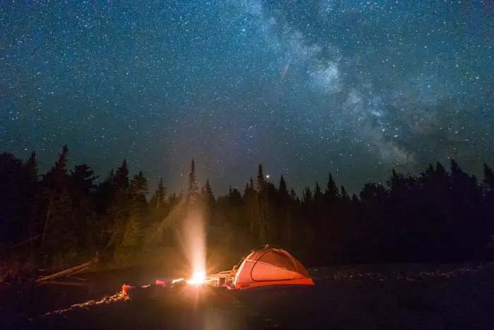 A tent and a campfire under a night sky bright with stars and the Milky Way.