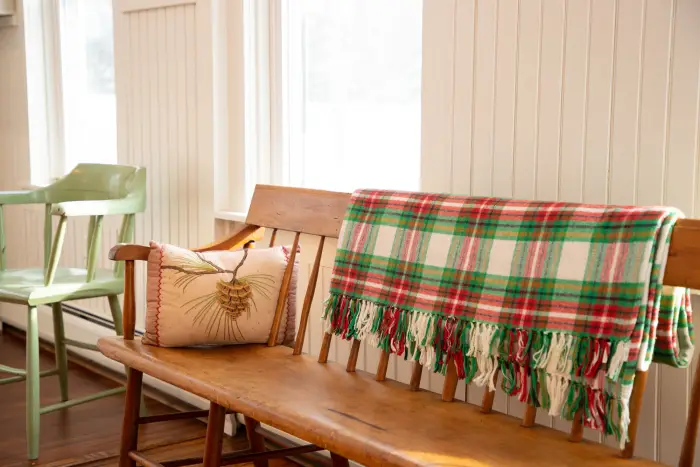 a bench with a checkered christmas blanket and a pinecone pillow.