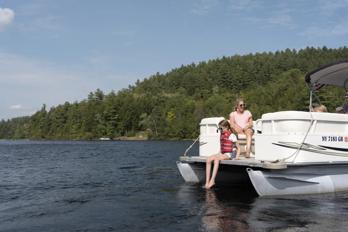 A woman and two children sit on a moving pontoon boat.