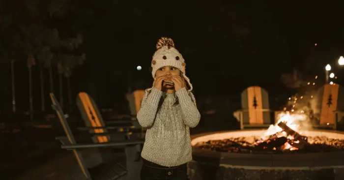 A child stands near a fire at The Lodge at Schroon Lake and eats a s'more