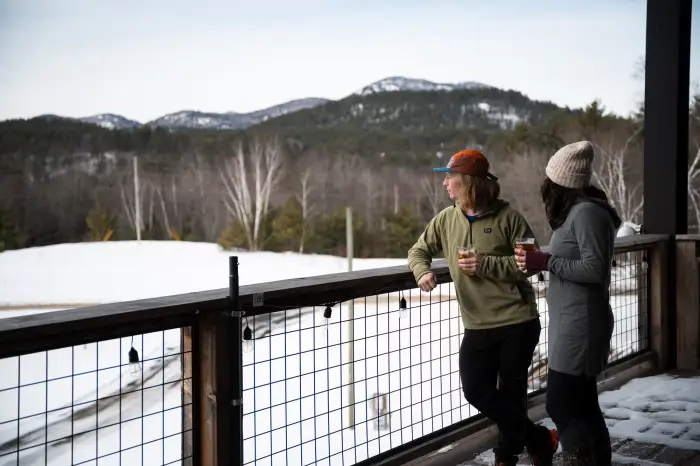 Two people drinking beer on the patio at Paradox Brewery with snowy mountains behind them.