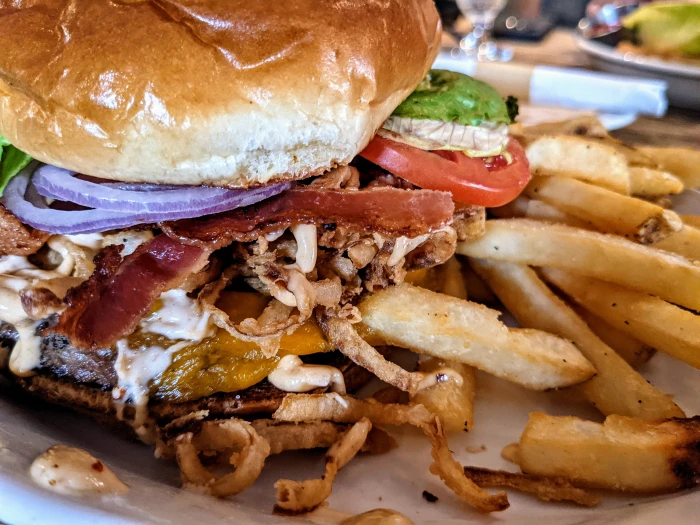 A close-up image of a burger topped with lettuce&#44; tomato&#44; onion&#44; and bacon with a crispy side of fries