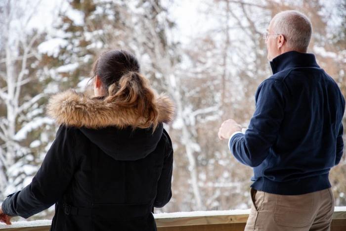 A couple wearing winter clothing looks out toward a snowy forest