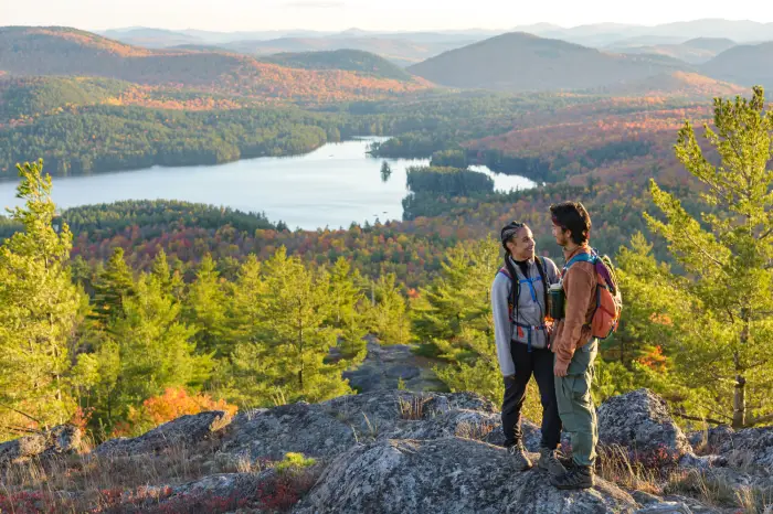 A couple standing on a mountain top looking at each other with fall foliage in the background.