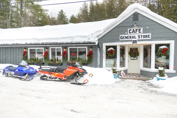 The Newcomb Cafe in the snow with wreaths decorating it and snowmobiles out front.
