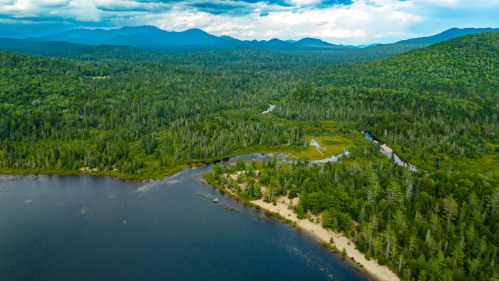 an aerial view of a marshfield&#44; lake&#44; and green mountain range in the background.