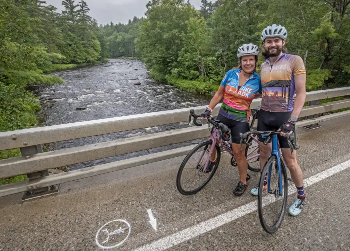 Two riders poses on their bikes in front of a river.