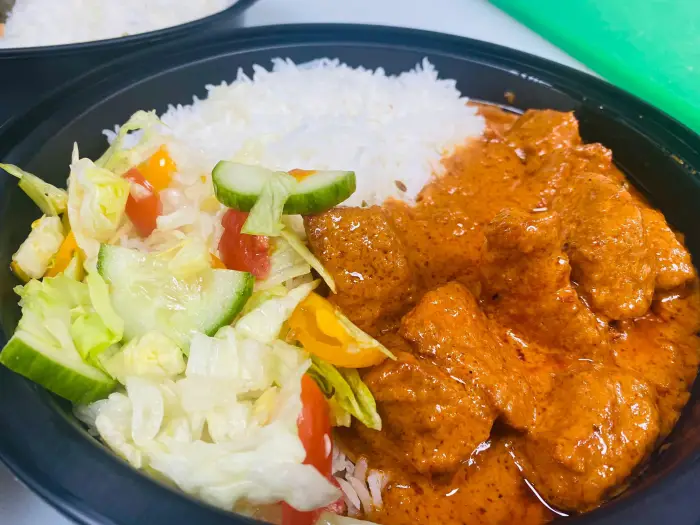 A plate of butter chicken&#44; rice&#44; and salad.