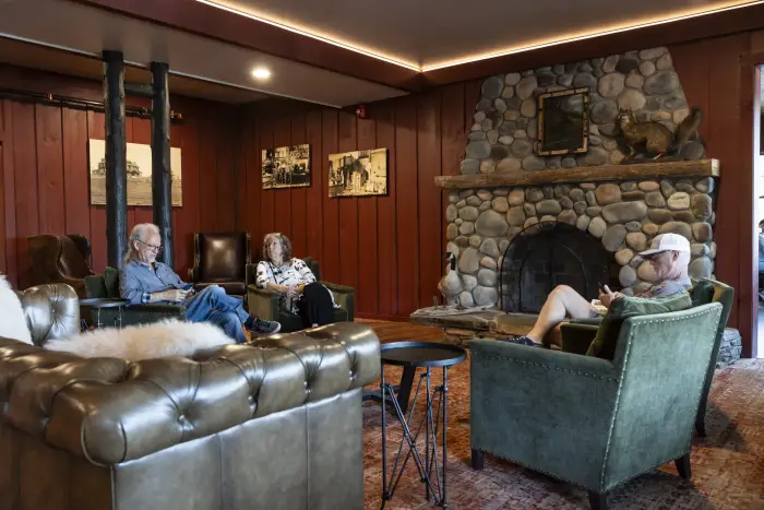 A hotel lounge with dark wood walls&#44; large stone fireplace&#44; and people sitting in plush leather couches.