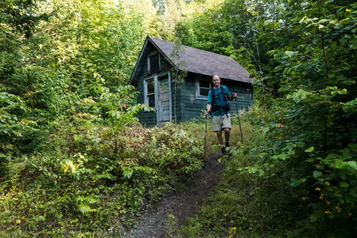 A man hikes by the old fire tower observer's cabin surrounded by forest.