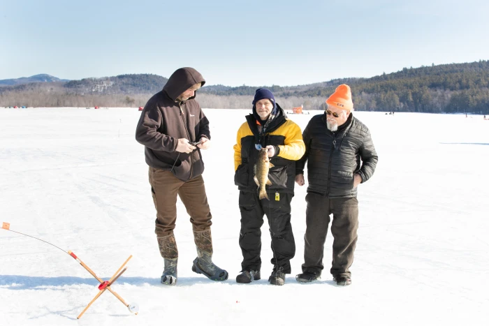 Three men stand on a frozen lake with a bass catch while ice fishing.