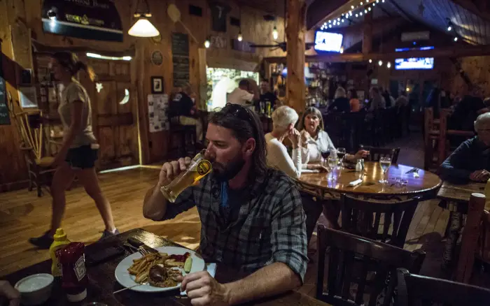 a man sips beer at a crowded lodge-style restaurant.