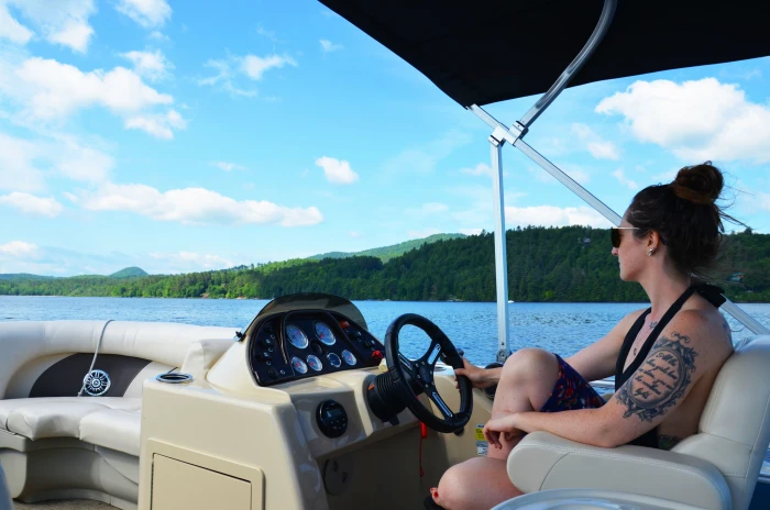 A woman in a bathing suit pilots a boat on an Adirondack lake.