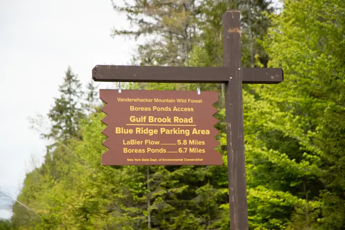 A Boreas River Tract sign painted in dark brown with yellow lettering stands in front of a backdrop of leafy forest.