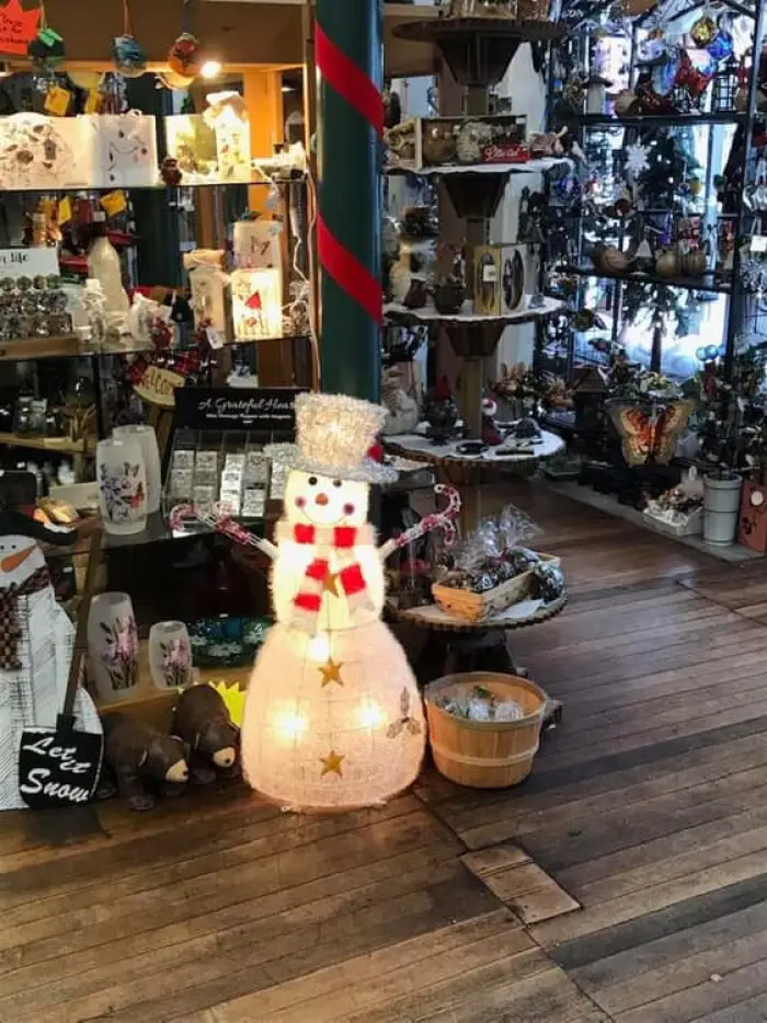 A jaunty&#44; lit snowman Christmas ornament stands in front of shelves stocked with Christmas decor.