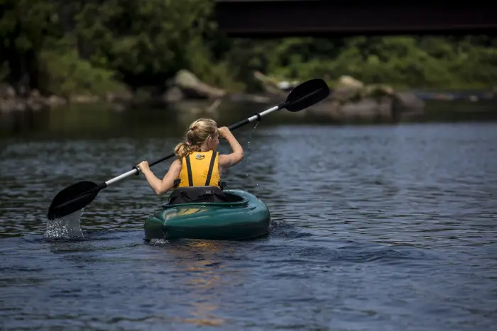 A girl paddles down a river in a teal kayak