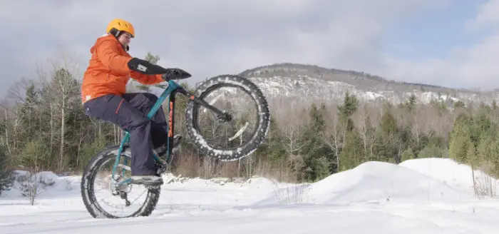 A person riding a fat tire bike does a wheelie in the snow