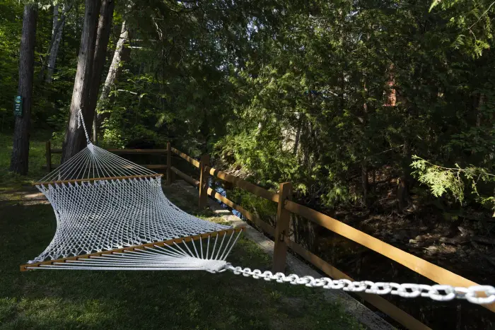 A hammock swings in between two trees next to a fence.