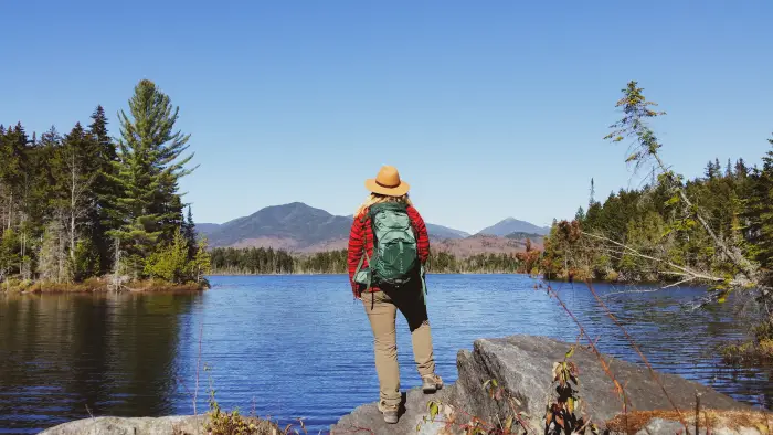 A woman standing on the shore of an Adirondack pond with High Peaks on the far shore.