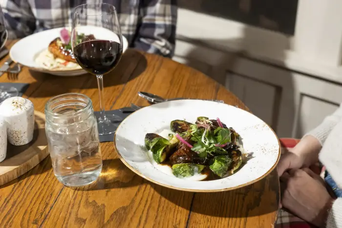 A couple sitting a table with a close up of their dinner dishes and glasses of wine.