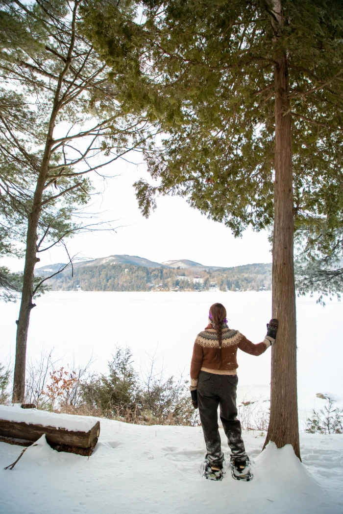 A woman stands in front of a frozen pond with snowy mountain views.