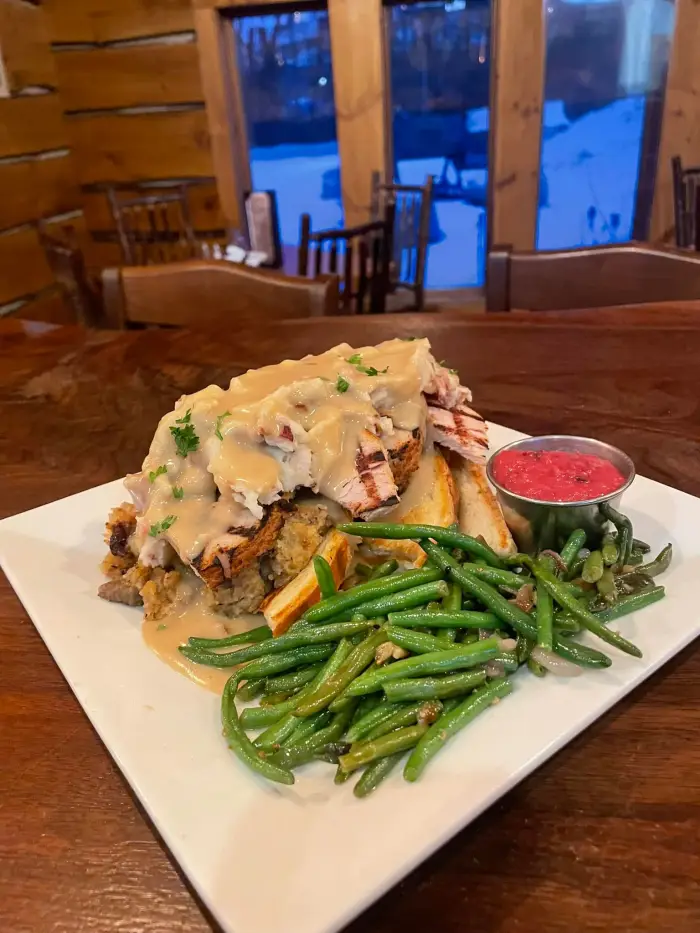 A plate of turkey&#44; mashed potatoes&#44; and beans on a wooden bar with a snowy view in the background.