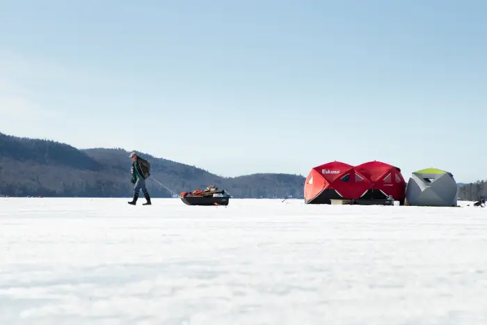 A man walks a sled of gear away from his ice fishing huts.
