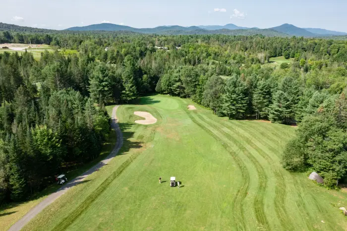 An aerial view of the High Peaks Golf Course with a fairway&#44; rough&#44; and sand trap&#44; and people playing a hole.