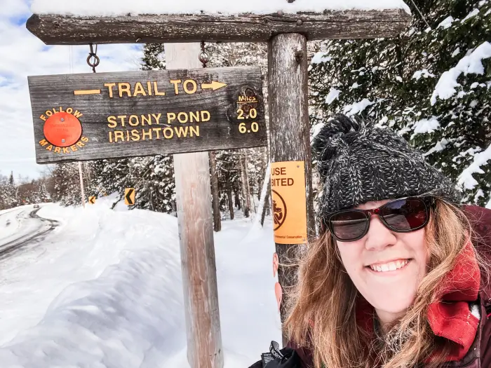 A woman smiling next to a trail sign.