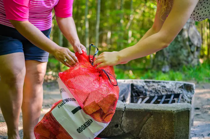 Two campers open a bag of firewood in front of a fire pit