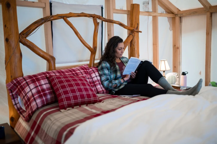 A woman sits on a bed while reading a book.