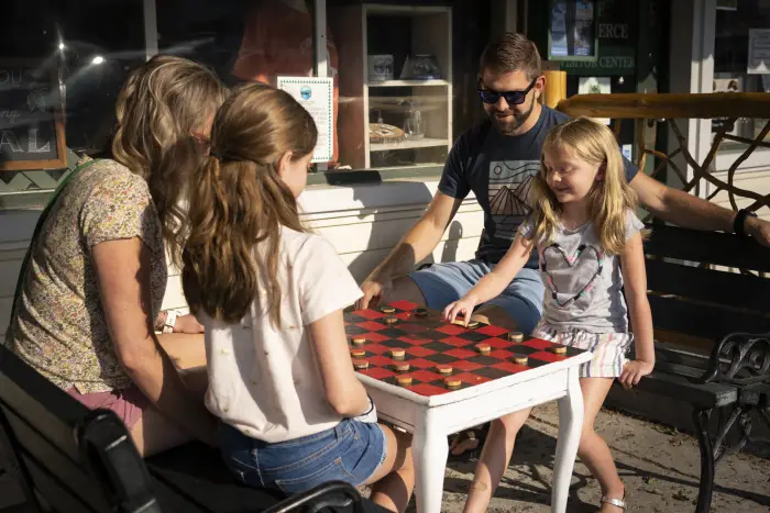 Two adults and two children enjoy a giant checkers game outside.