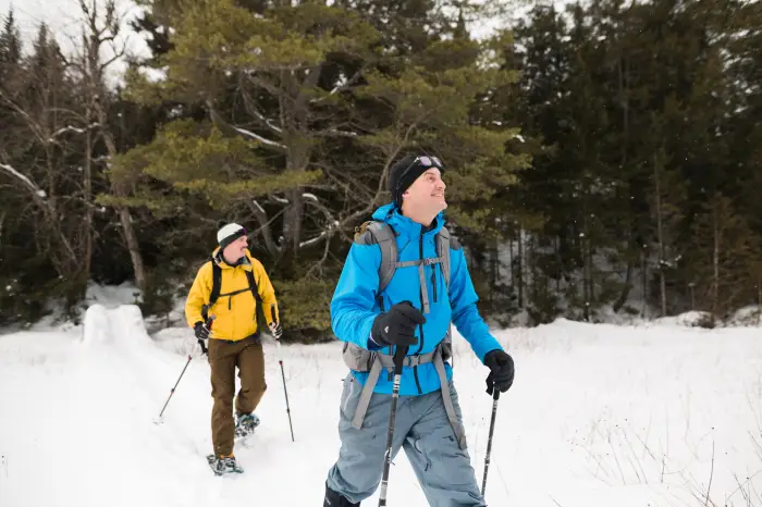 Two men use walking sticks to snowshoe through the snow.