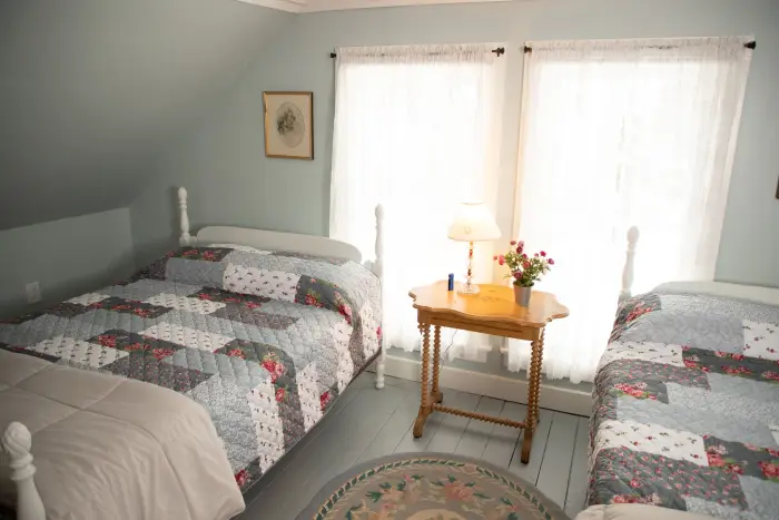 two beds in a light blue room with end table in the middle.
