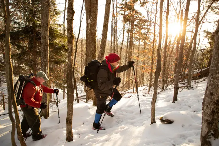 Two people hiking up a snowy trail during sunset.