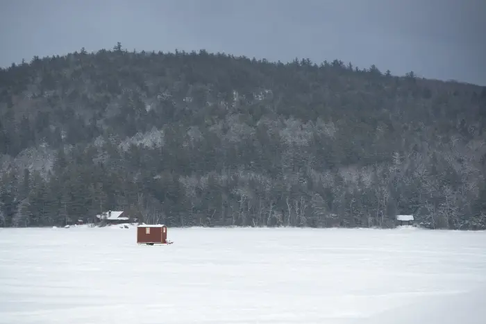 A shanty on a frozen lake with a distant hill covered in trees.