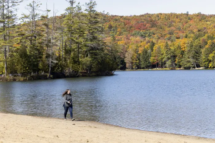 A hiker in motin on the sand of Donnelly beach&#44; with a backdrop of autumn color and reflections in the water