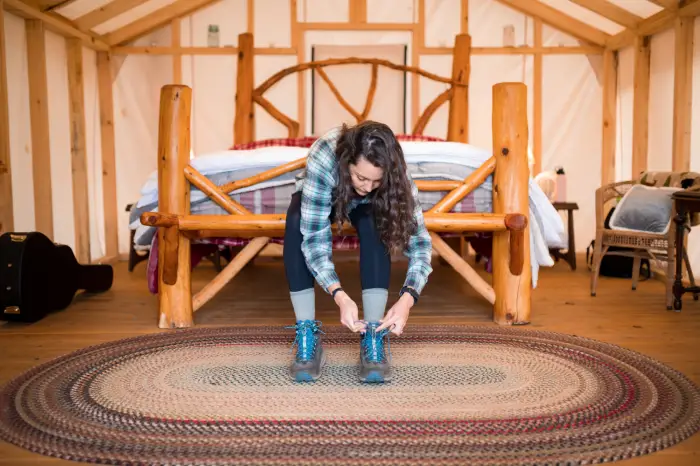 A woman ties her boots while sitting on a bench inside a large tent