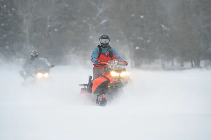 Two snowmobiles traveling through a flurry of snowflakes.