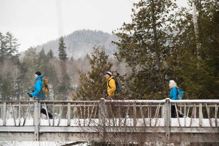 Three adults cross a wooden pedestrian bridge over a frozen lake.