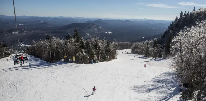 View from the chairlift of two ski trails with people skiing down them and distant snowy mountains