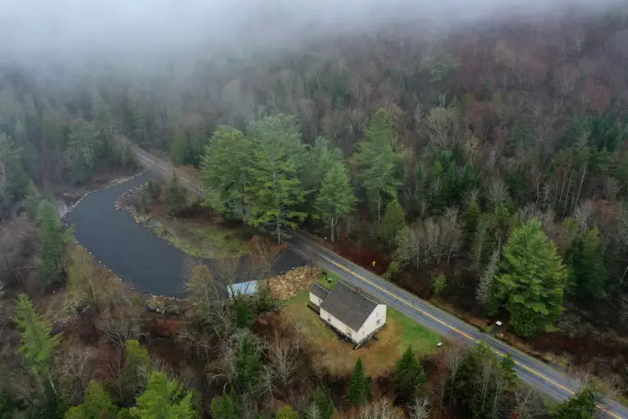 An aerial view of an old house alongside a road&#44; surrounded by forest.
