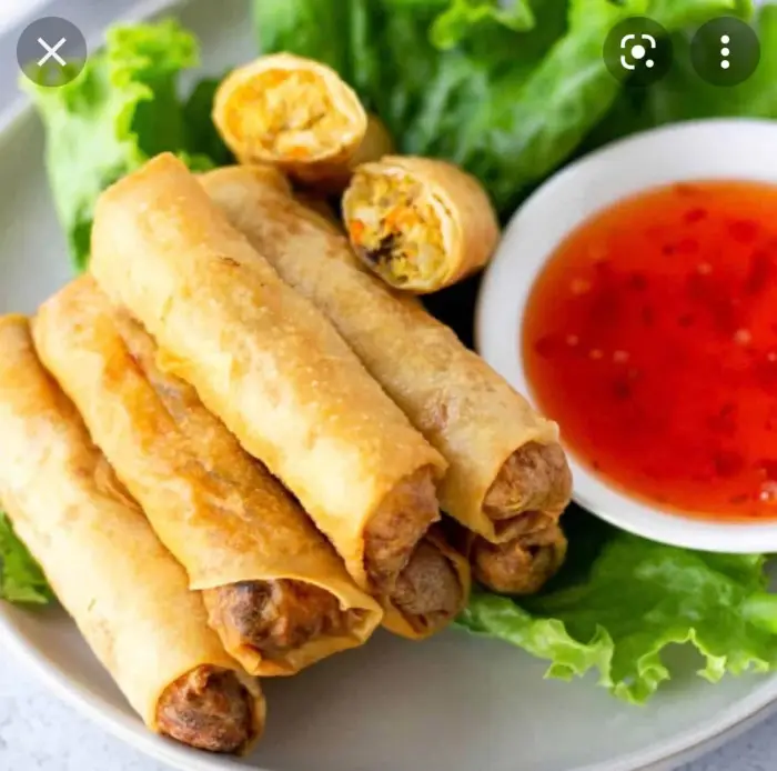 A plate of freshly cooked chicken spring rolls next to an orange-colored dipping sauce.