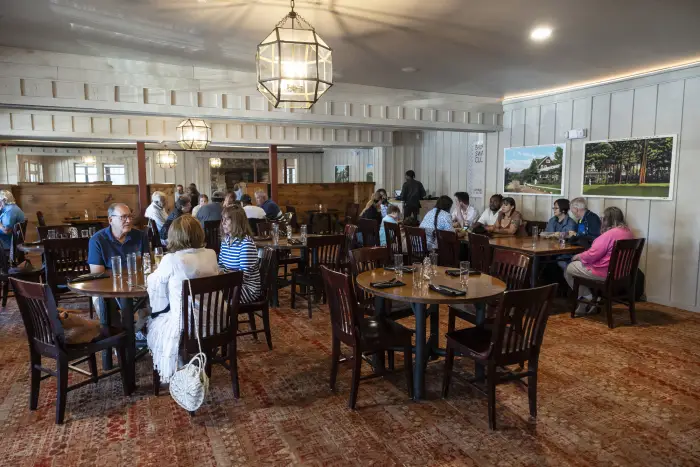 Diners sit at square tables in a cozy Adirondack restaurant with Adirondack camp-style decor.